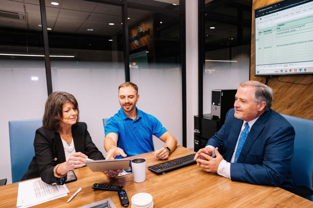 Three people at a table discussing CMMC 2.0 requirements.