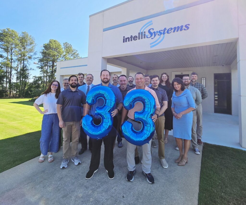 IntelliSystems team standing in front of building with balloons in the shape of "33".
